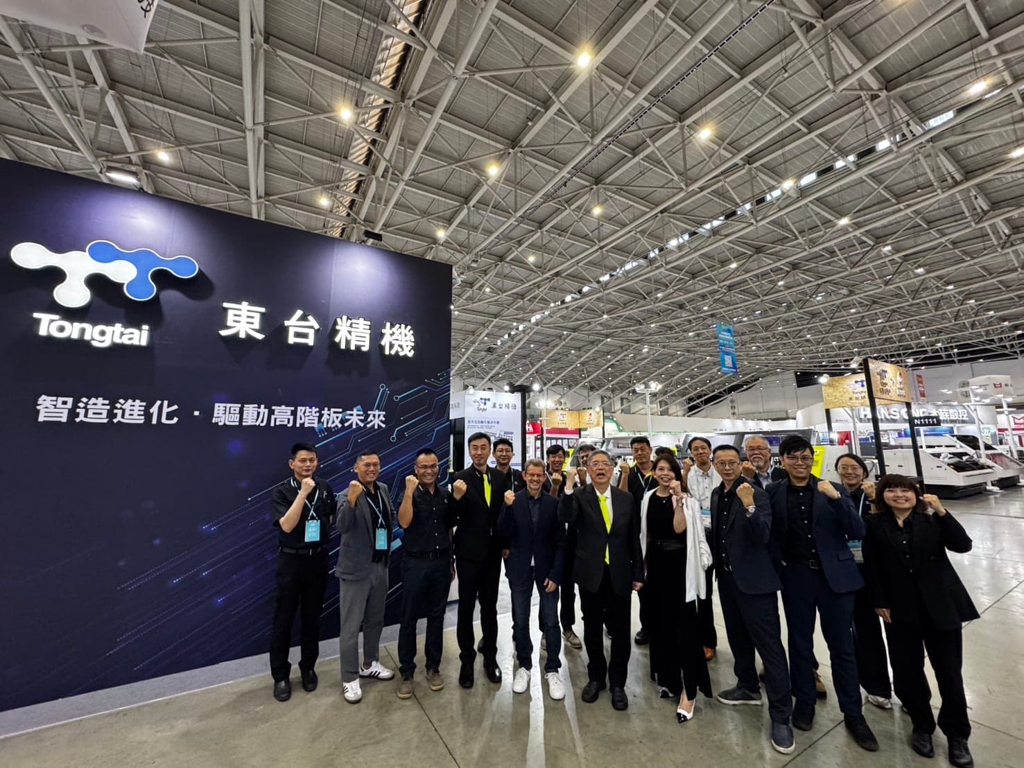 東台精機董事長嚴瑞雄（前排右五）率領團隊與海內外合作夥伴於 TPCA Show 2026 展位前合影。東台透過高精度鑽孔設備結合 AMR 自動化物流調度，協助全球高階板廠突破鑽孔製程瓶頸，共同推進 PCB 製造智慧化轉型。（圖/東台提供）